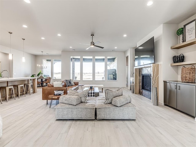 living room featuring a ceiling fan, light wood-type flooring, a fireplace, and recessed lighting