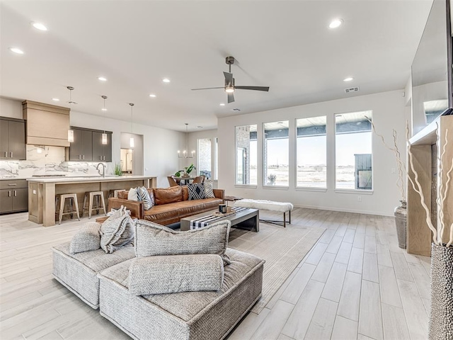 living area featuring light wood-type flooring, recessed lighting, baseboards, and ceiling fan with notable chandelier