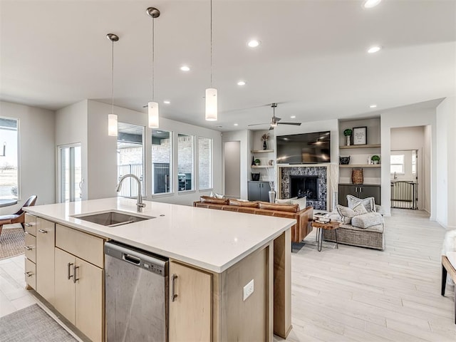 kitchen featuring a fireplace, recessed lighting, stainless steel dishwasher, a kitchen island with sink, and a sink