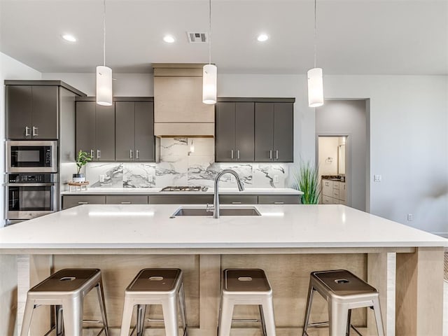 kitchen with a breakfast bar, stainless steel appliances, visible vents, decorative backsplash, and a sink