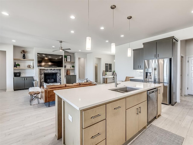 kitchen featuring appliances with stainless steel finishes, light countertops, light wood-type flooring, a fireplace, and a sink