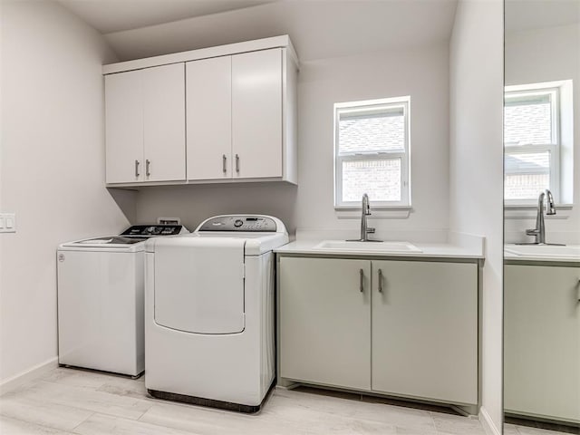 clothes washing area with baseboards, a sink, cabinet space, and washer and dryer