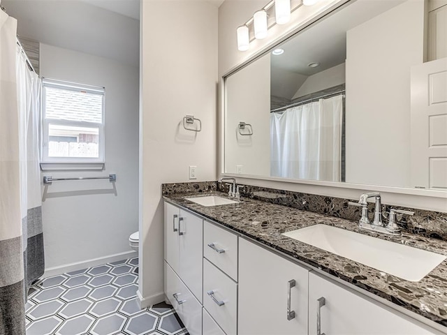 bathroom featuring baseboards, a sink, toilet, and double vanity