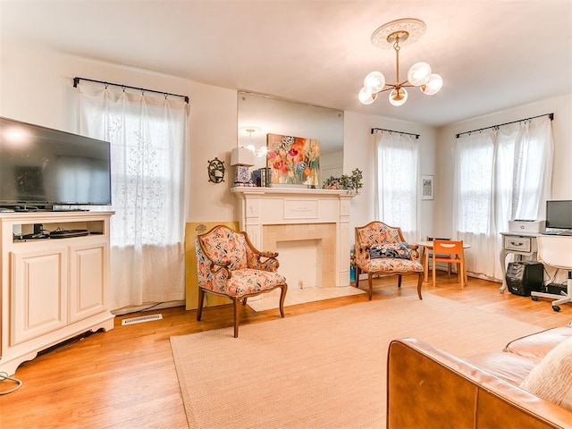 living room with a fireplace with flush hearth, visible vents, light wood finished floors, and an inviting chandelier