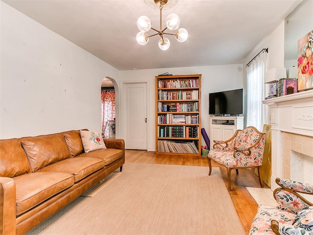 living area featuring an inviting chandelier, light wood-style flooring, arched walkways, and a tiled fireplace