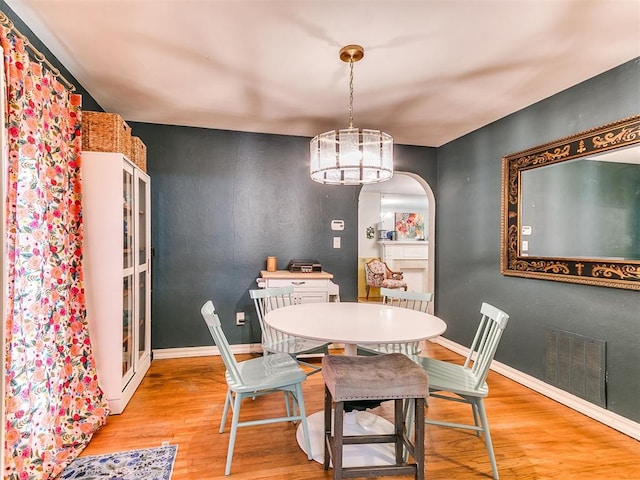 dining room with arched walkways, wood finished floors, visible vents, and baseboards