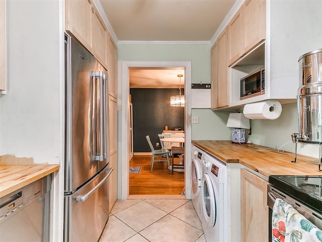 kitchen with light tile patterned floors, butcher block counters, ornamental molding, stainless steel appliances, and washer and dryer