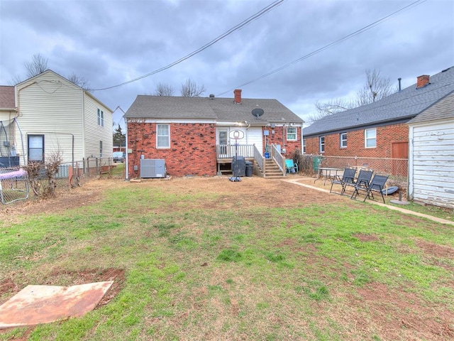 rear view of house featuring brick siding, fence private yard, central AC unit, and a yard