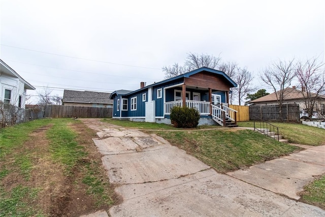 view of front facade with a chimney, a porch, a front yard, fence, and driveway