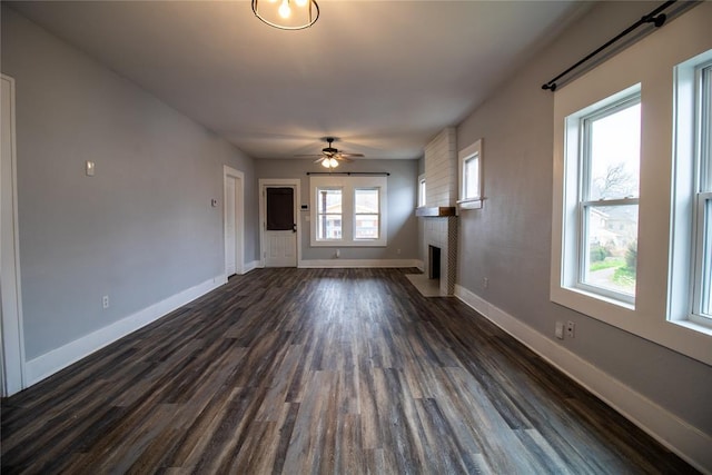 unfurnished living room featuring ceiling fan, a fireplace, baseboards, and dark wood-style flooring