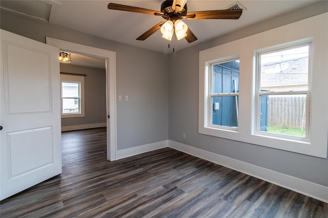 empty room with a ceiling fan, dark wood finished floors, plenty of natural light, and baseboards