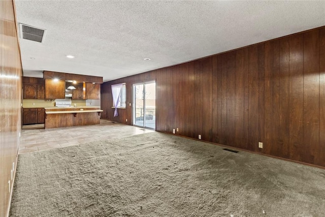 unfurnished living room featuring light carpet, visible vents, wood walls, and a textured ceiling