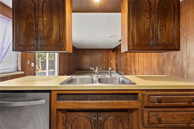 kitchen featuring a sink, stainless steel dishwasher, wood walls, and light countertops