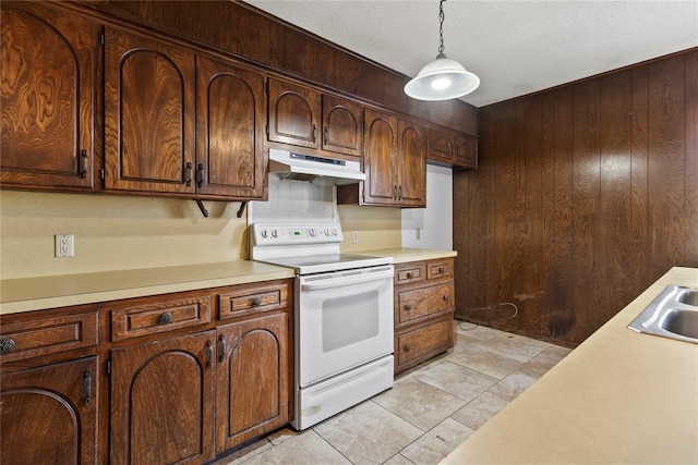 kitchen with under cabinet range hood, decorative light fixtures, wood walls, light countertops, and electric range