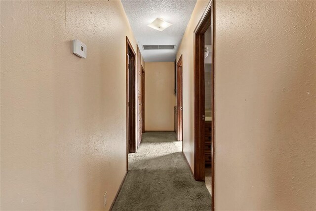 hallway featuring visible vents, carpet floors, a textured ceiling, and a textured wall