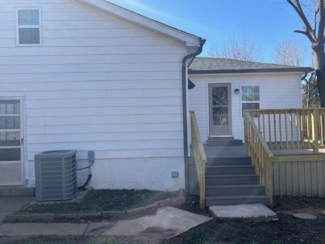 doorway to property featuring a shingled roof, central AC, and a wooden deck