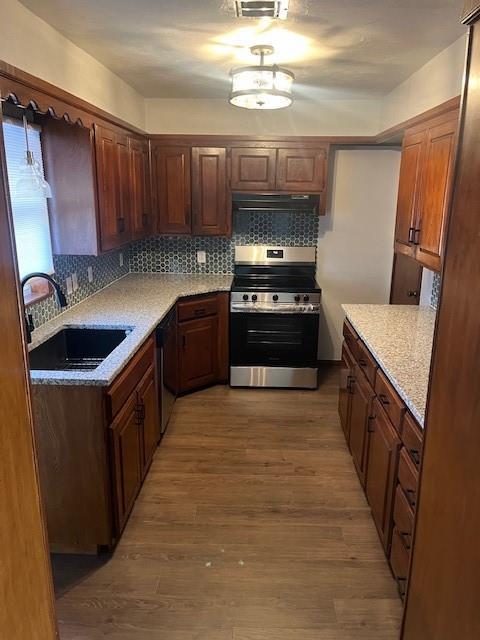 kitchen featuring light wood-style flooring, decorative backsplash, a sink, and stainless steel range with electric cooktop