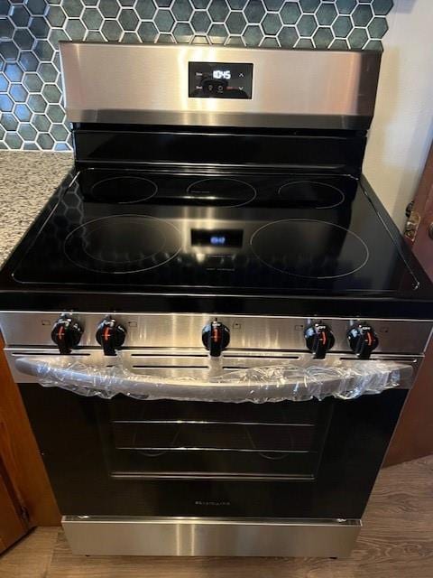 details with light wood finished floors, stainless steel electric range oven, light countertops, and backsplash