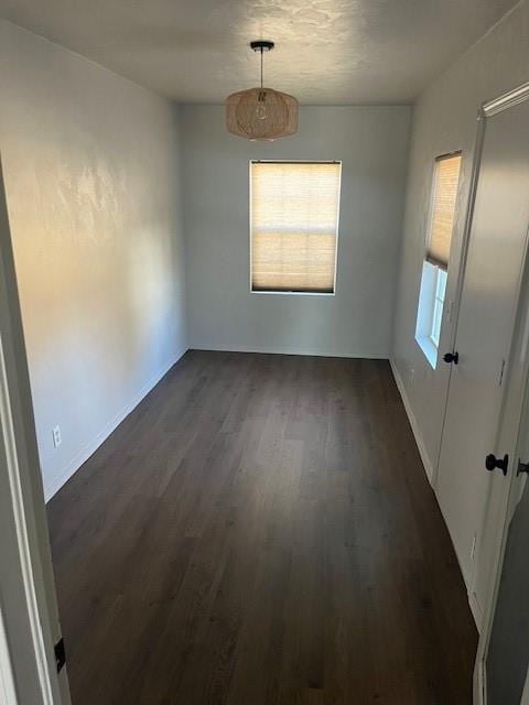 unfurnished dining area featuring dark wood-type flooring and baseboards