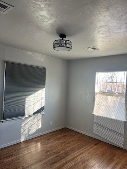 spare room featuring wood finished floors, visible vents, and baseboards