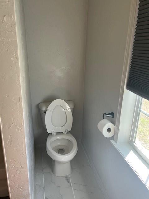 bathroom with marble finish floor, baseboards, a textured wall, and toilet