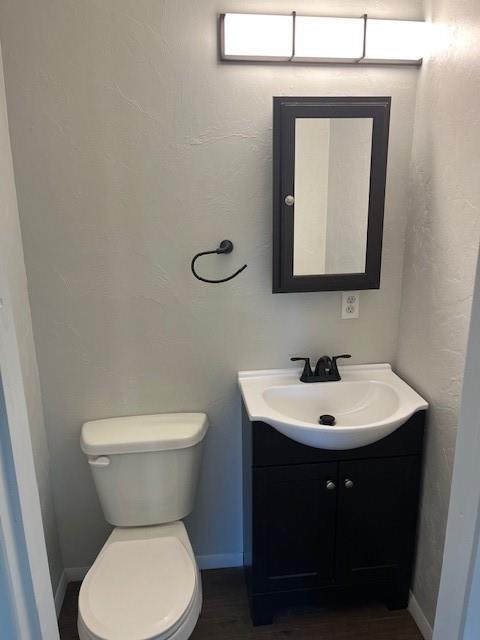 bathroom featuring baseboards, vanity, toilet, and wood finished floors