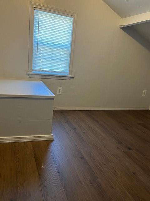 empty room featuring lofted ceiling, baseboards, and dark wood-type flooring