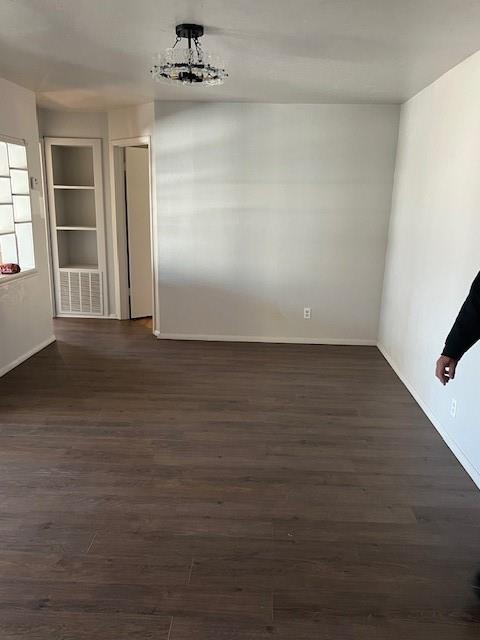 unfurnished room with baseboards, visible vents, and dark wood-style flooring