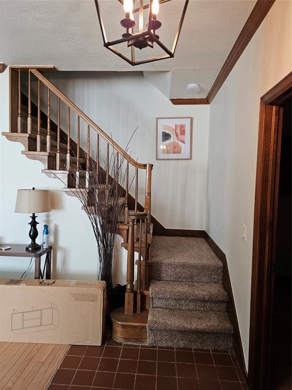 staircase featuring a textured ceiling, crown molding, baseboards, and a chandelier