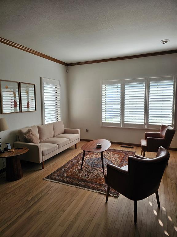 living area featuring wood finished floors, a textured ceiling, and ornamental molding