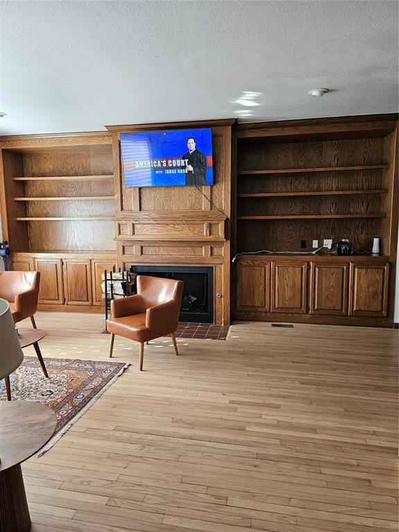 living area featuring built in features, a fireplace, a textured ceiling, and light wood-type flooring