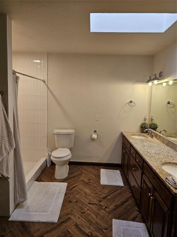 full bath with a tile shower, toilet, a skylight, and a sink