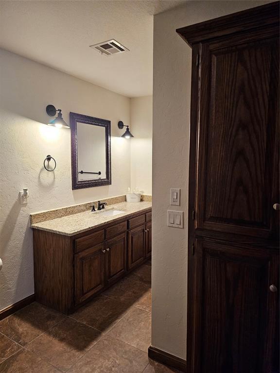 bathroom with visible vents, vanity, baseboards, and a textured wall