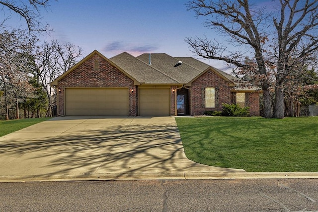 view of front facade featuring a shingled roof, concrete driveway, a front yard, an attached garage, and brick siding