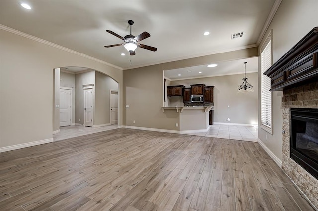 unfurnished living room featuring visible vents, light wood-style flooring, arched walkways, a stone fireplace, and ceiling fan