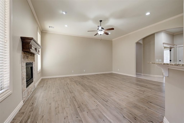 unfurnished living room with visible vents, a stone fireplace, light wood-style floors, arched walkways, and a ceiling fan