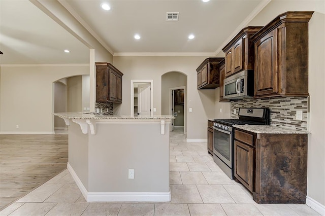 kitchen featuring visible vents, a peninsula, arched walkways, stainless steel appliances, and a kitchen bar