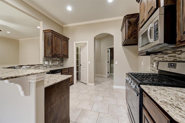 kitchen with ornamental molding, light stone counters, arched walkways, appliances with stainless steel finishes, and dark brown cabinets