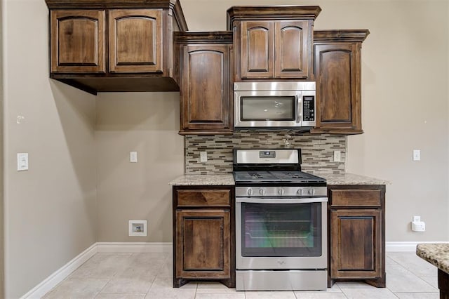 kitchen with stainless steel appliances, light stone countertops, backsplash, and dark brown cabinetry