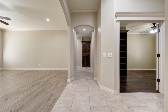 hall with light tile patterned floors, baseboards, arched walkways, and crown molding