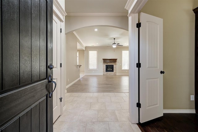 entryway featuring crown molding, baseboards, a fireplace, arched walkways, and a ceiling fan