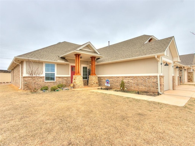 view of front facade featuring a garage, a front yard, brick siding, and roof with shingles