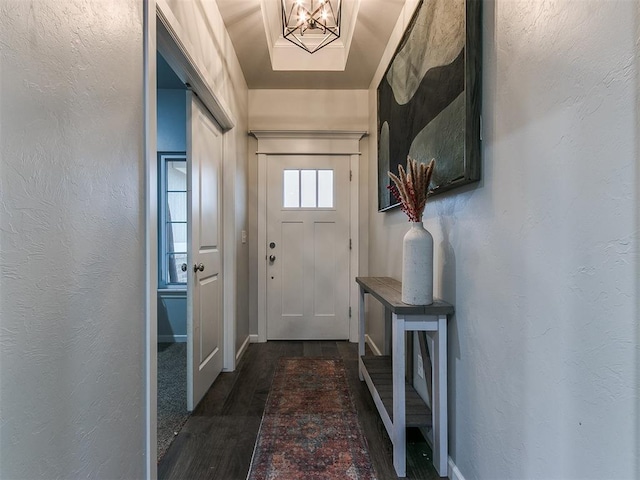 entryway with dark wood-style flooring, a notable chandelier, and a textured wall