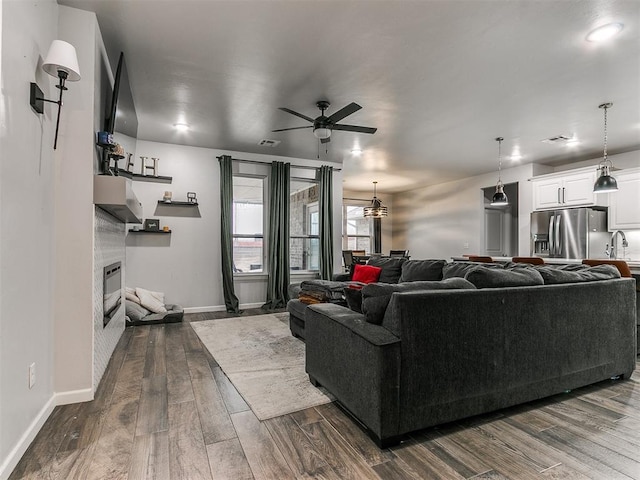 living area featuring dark wood-style floors, a tiled fireplace, a ceiling fan, and baseboards