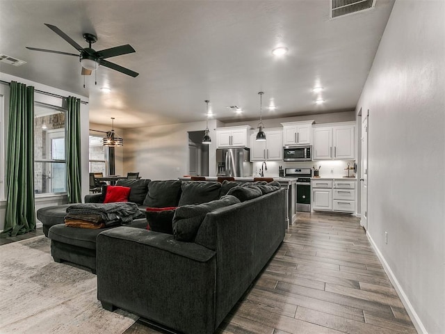 living room with dark wood-style flooring, visible vents, baseboards, and ceiling fan with notable chandelier