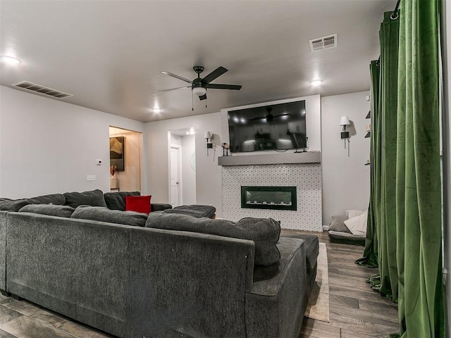 living room with ceiling fan, a fireplace, visible vents, and wood finished floors