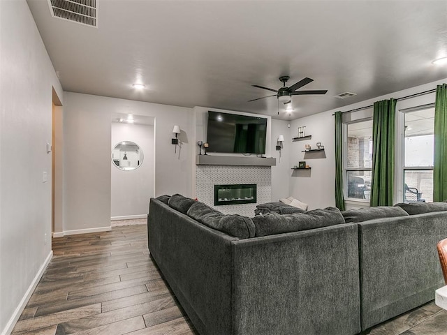 living area with a ceiling fan, visible vents, a fireplace, and wood finished floors