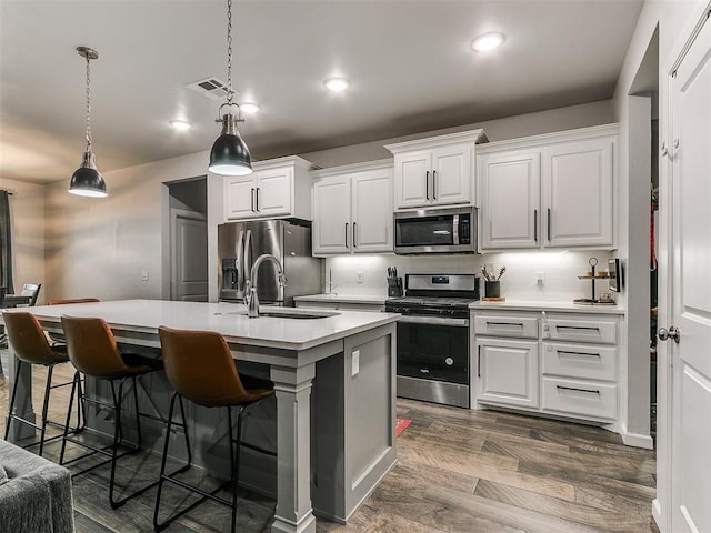 kitchen featuring a center island with sink, stainless steel appliances, light countertops, visible vents, and a sink