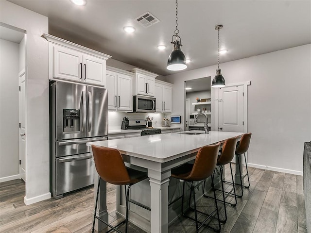 kitchen featuring dark wood-type flooring, a sink, appliances with stainless steel finishes, a kitchen bar, and a center island with sink