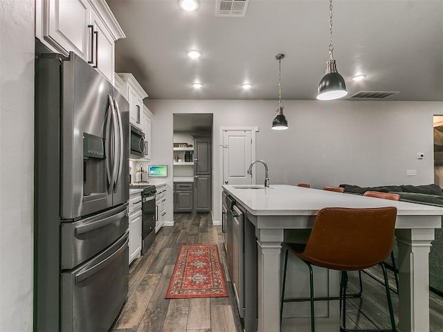 kitchen featuring stainless steel appliances, a sink, visible vents, light countertops, and dark wood finished floors